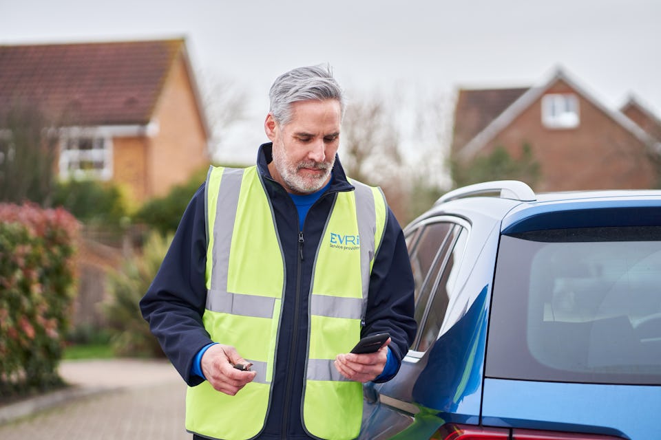 male courier stood next to blue car using smartphone