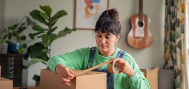 woman sat at table applying brown tape to cardboard box