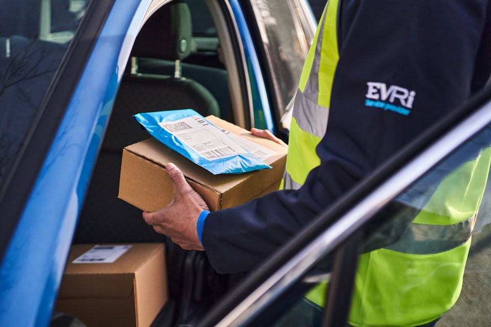 Courer outside blue van holding a box and packet