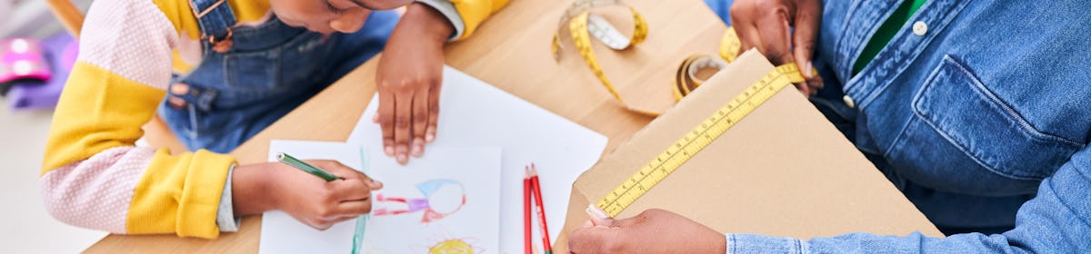 woman holding tape measure to cardboard box while child draws sitting next to her