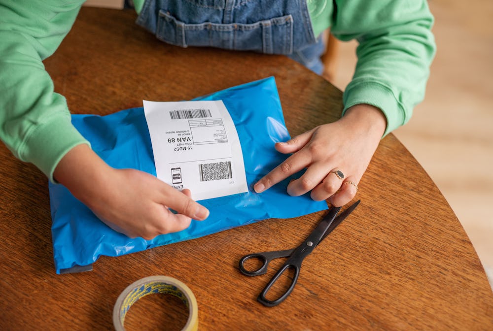 woman placing label on blue parcel bag while sat at table