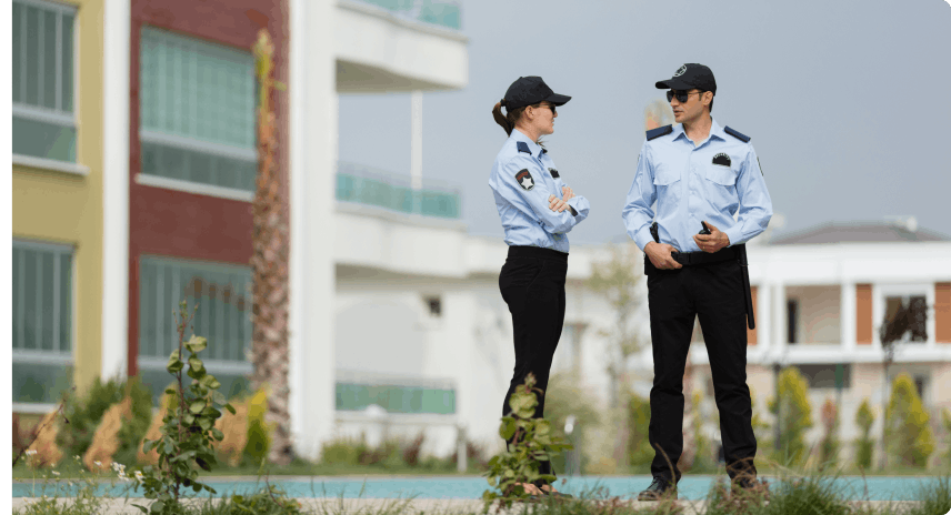 Two security guards, one man, one woman, protect the neighborhood of a municipality, pool and modern apartments in the background