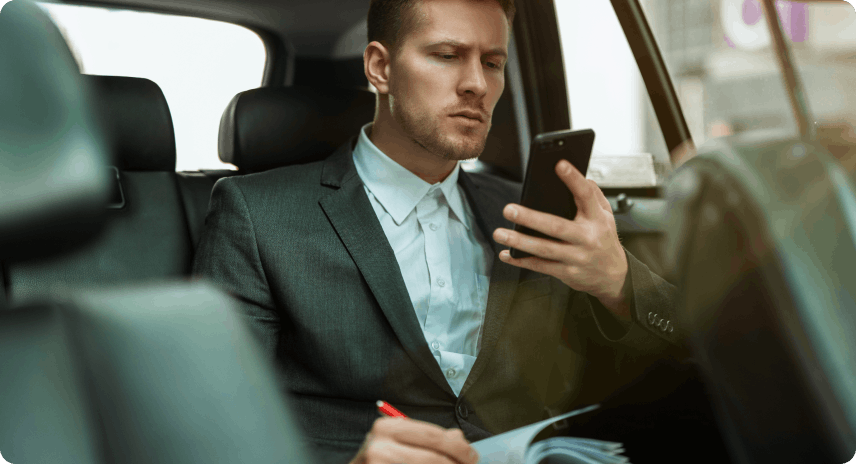 Young modern businessman in the back seat of a car looking at his phone