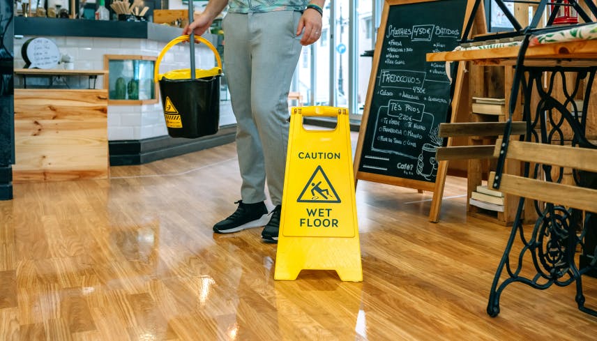 Man in a cafe cleaning with a mop, caution sign warning about the wet floor  