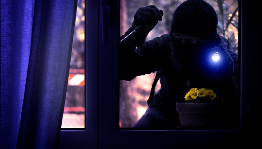 Burglar with flashlight trying to break in through a window in the middle of the night