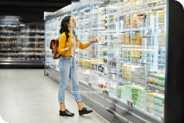 Woman in a bright yellow sweater selecting products from a cooling shelf in an autonomous supermarket at night
