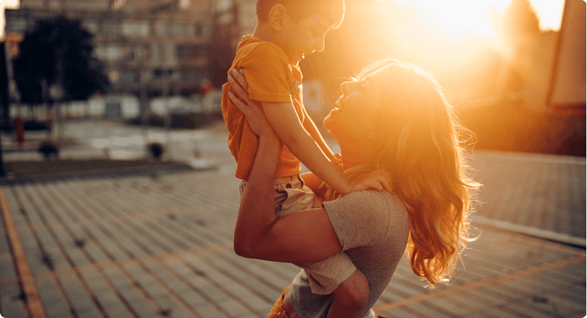 Junge Mutter und Sohn spielen im Freien und haben Spass, während die Sonne untergeht und die Szene in ein goldenes Licht taucht