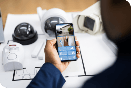 Installer looking at video surveillance footage on his smartphone with a desk full of security cameras