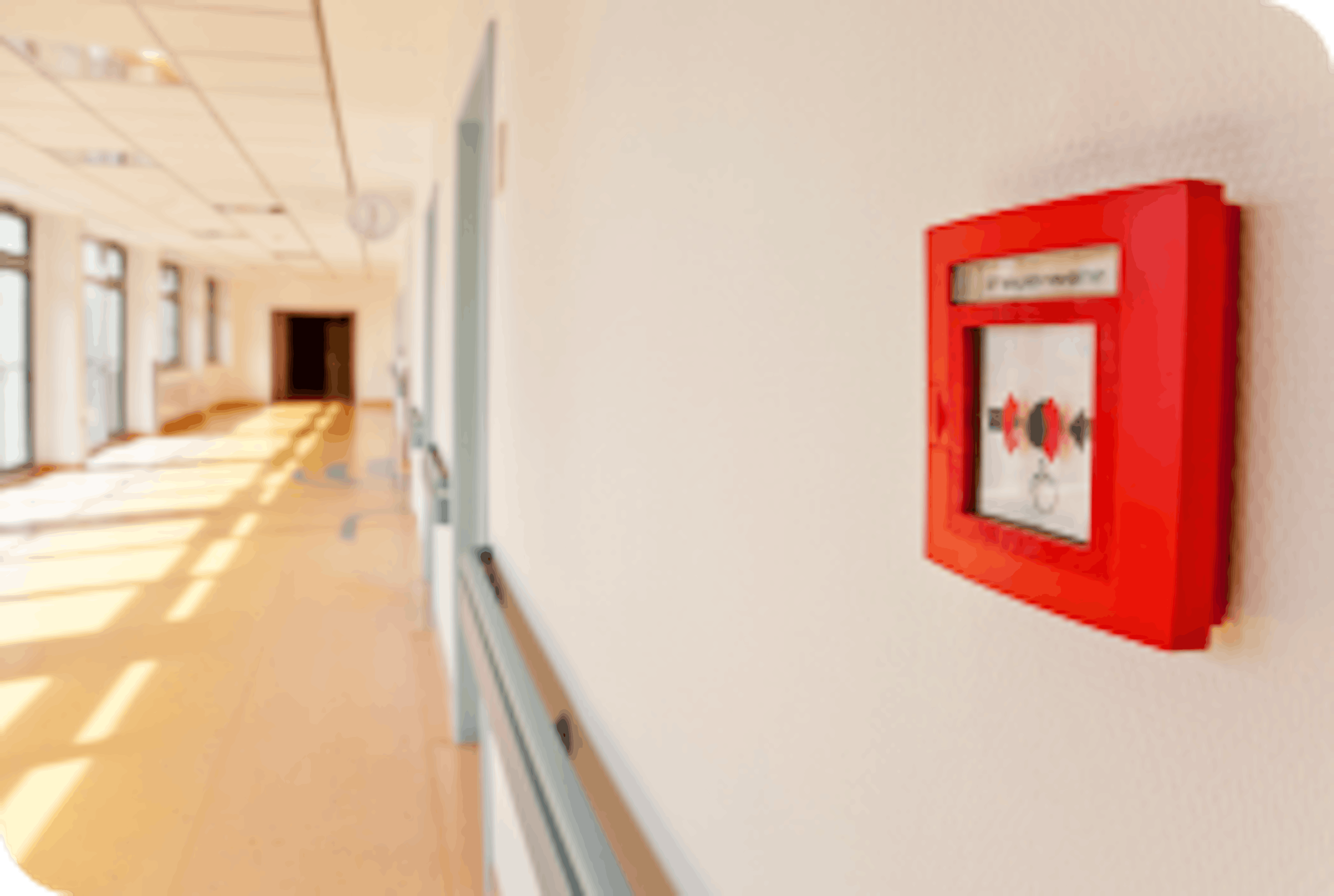 Red fire alarm mounted on a wall in a school building