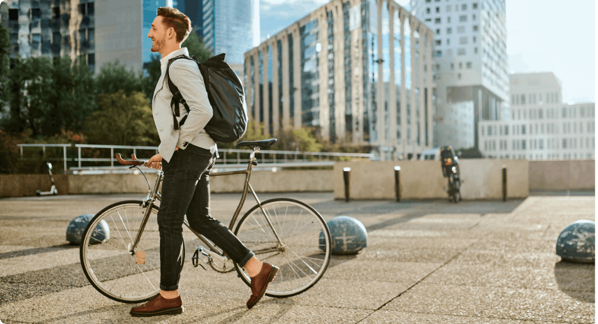 Aufnahme eines jungen geschäftsmannes, der mit seinem fahrrad und einem Rucksack lächelnd durch die Stadt fährt