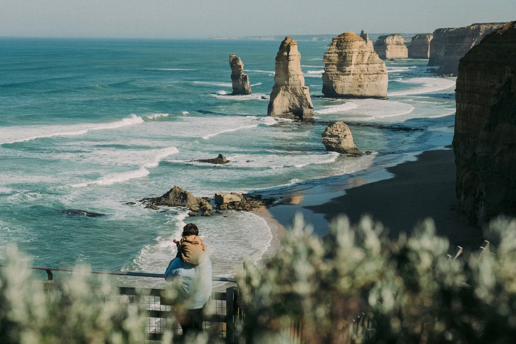 Un père portant son enfant sur les épaules face aux Douze Apôtres, en Australie