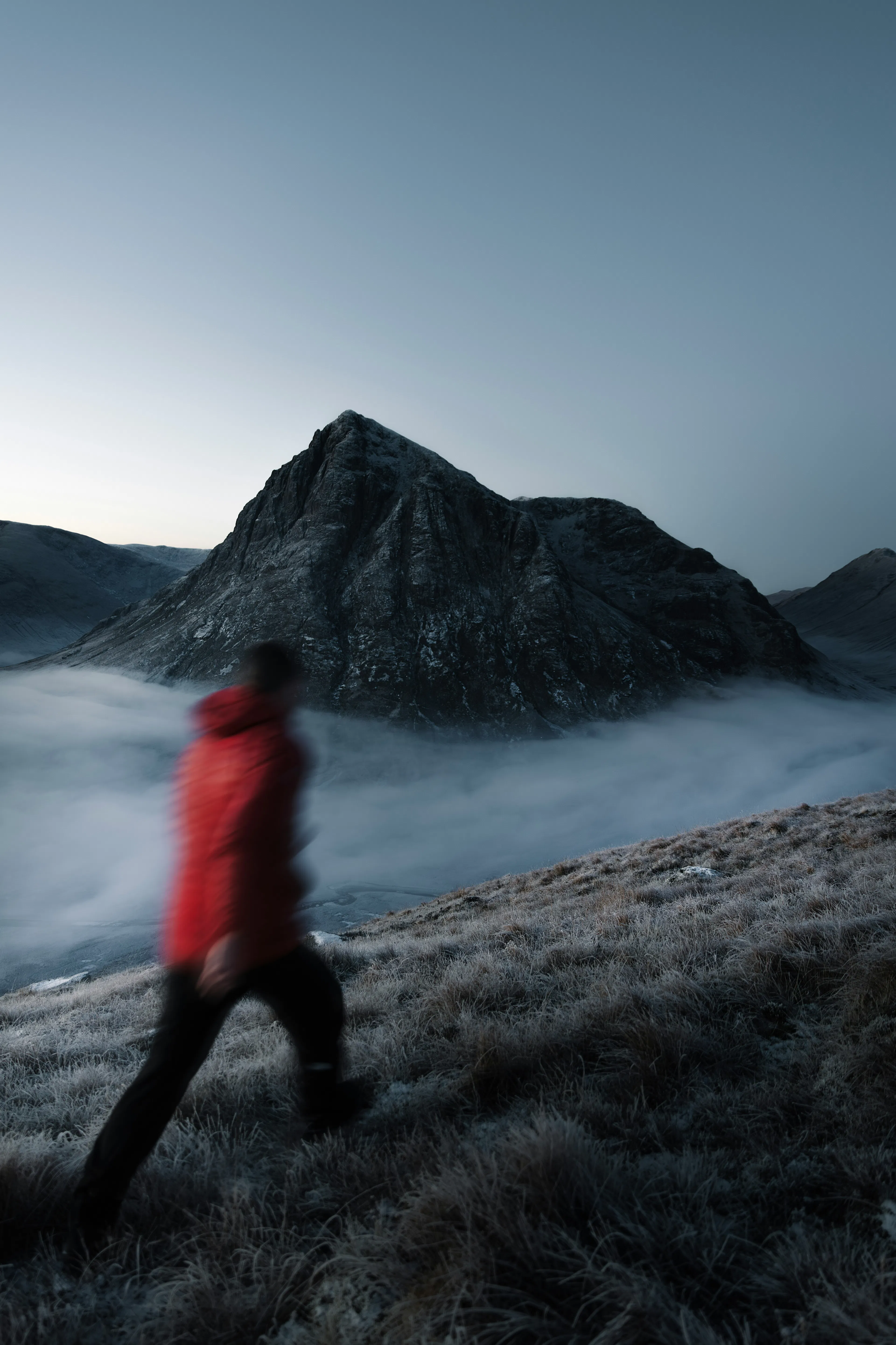 Un homme en veste rouge marchant dans la brume des montagnes écossaises
