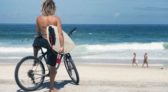 Surfeur sur son vélo, la planche à la main, face à la plage de Copacabana