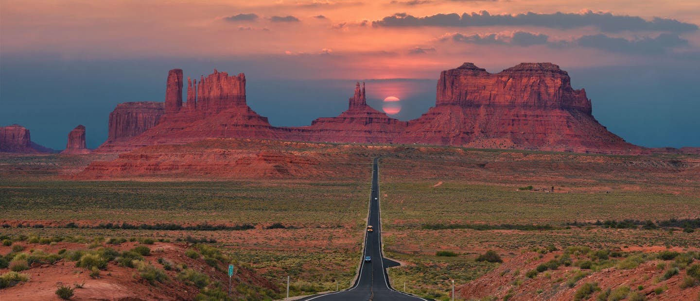 Route filant à travers Monument Valley sur fond de coucher de soleil.