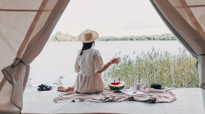 Jeune femme de dos pique-niquant devant une tente face à un lac