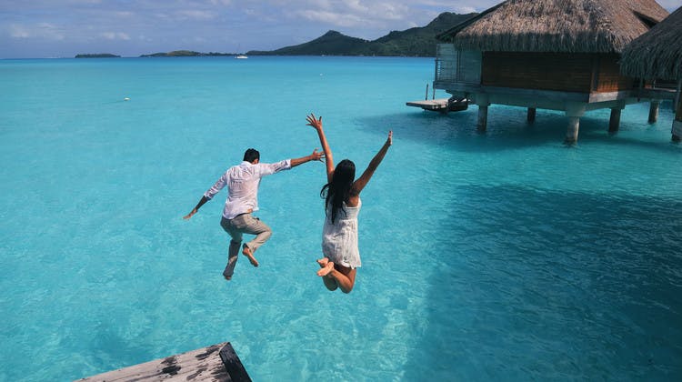Couple sautant dans l'eau turquoise d'un lagon polynésien