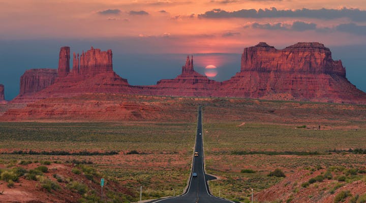 Route filant à travers Monument Valley sur fond de coucher de soleil.