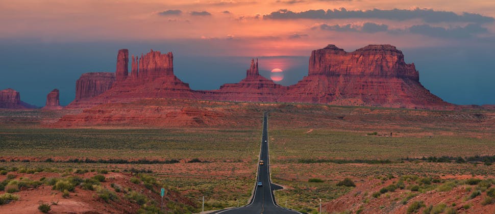 Route filant à travers Monument Valley sur fond de coucher de soleil.