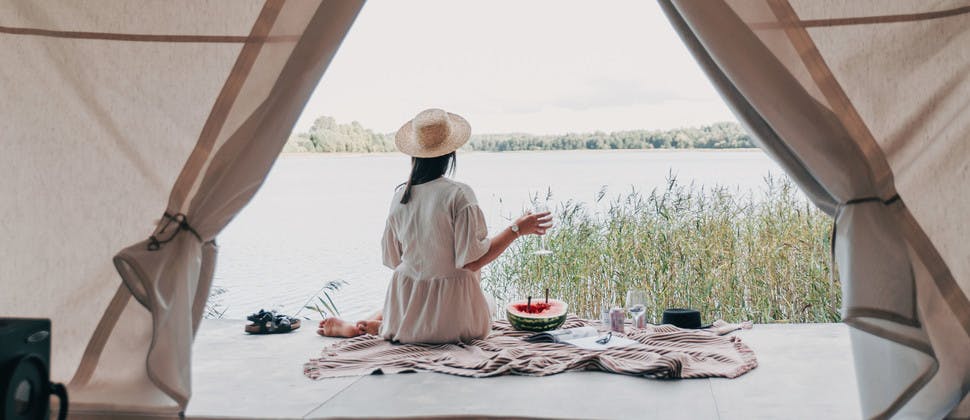 Jeune femme de dos pique-niquant devant une tente face à un lac