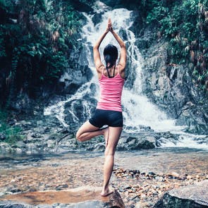 Junge Frau macht Yoga vor einem Wasserfall