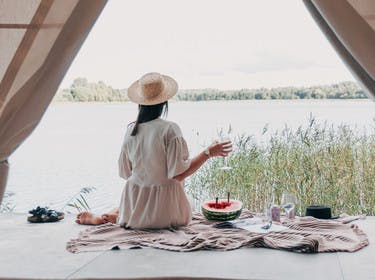 Jeune femme de dos pique-niquant devant une tente face à un lac