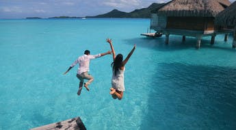 Couple sautant dans l'eau turquoise d'un lagon polynésien