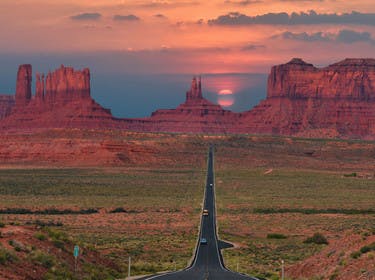 Route filant à travers Monument Valley sur fond de coucher de soleil.
