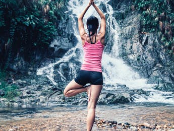 Junge Frau macht Yoga vor einem Wasserfall