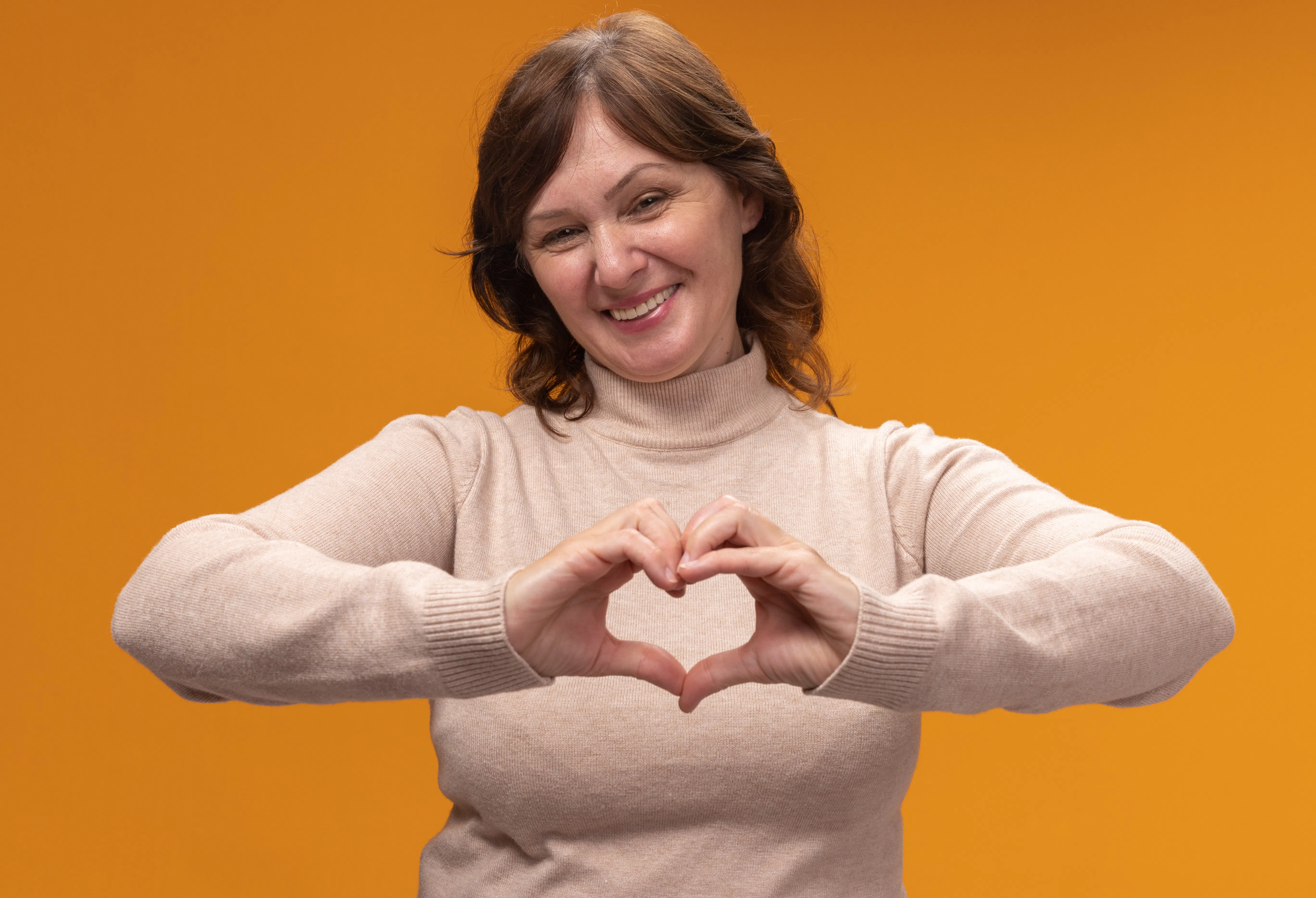 Midlife woman smiling and making a heart shape with her hands, representing heart health awareness and self-love during menopause