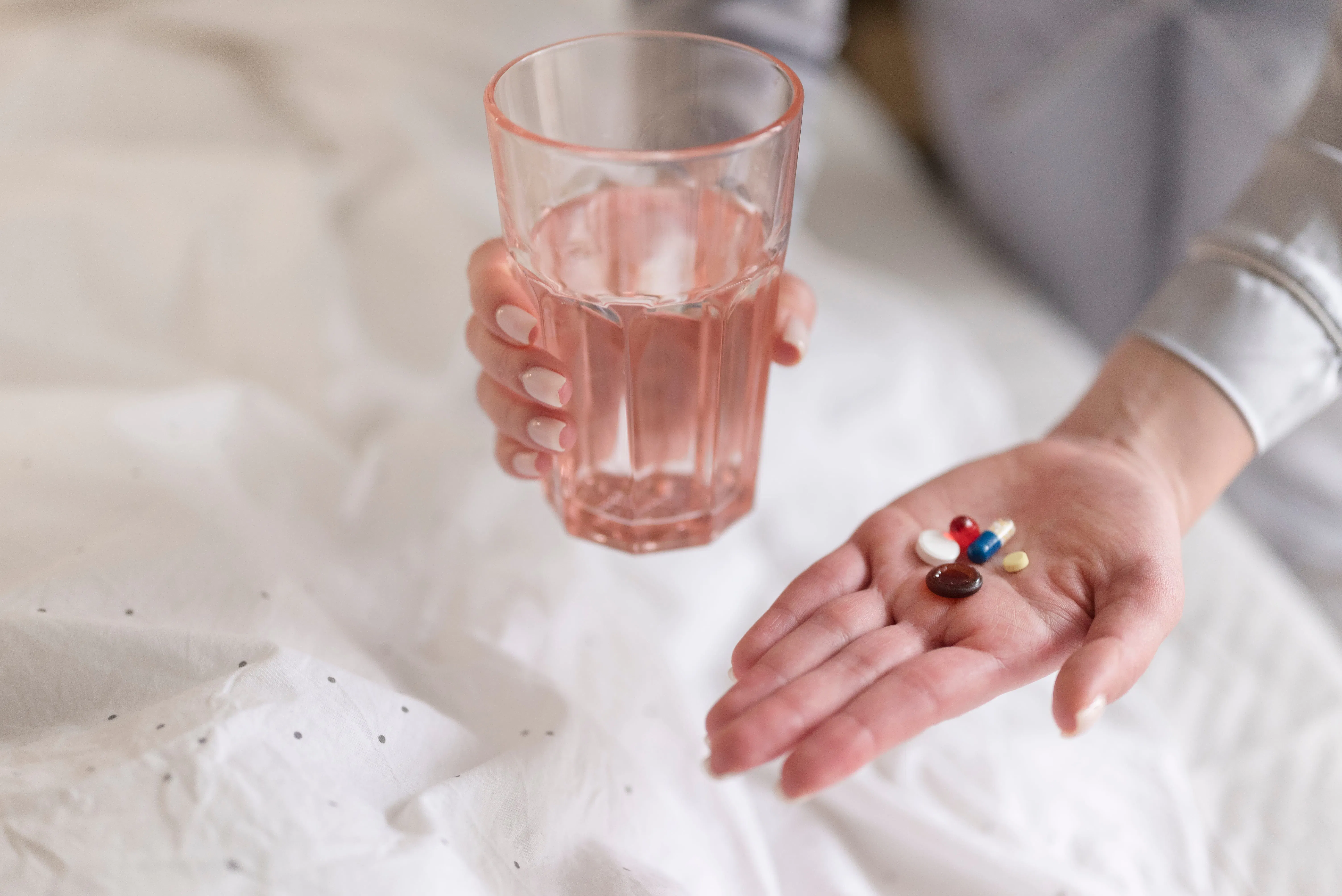 Close-up of a hand holding essential supplements and a glass of water, illustrating a mindful approach to vitamins and minerals during menopause.