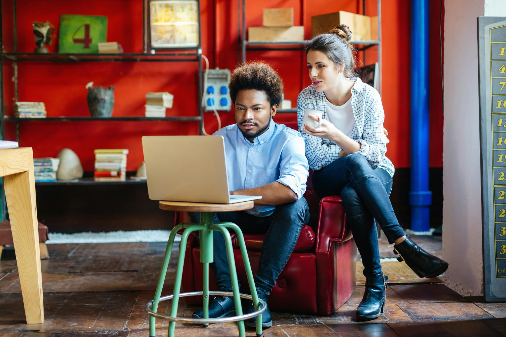 Two people are sitting at a cafe, looking at the laptop screen together.