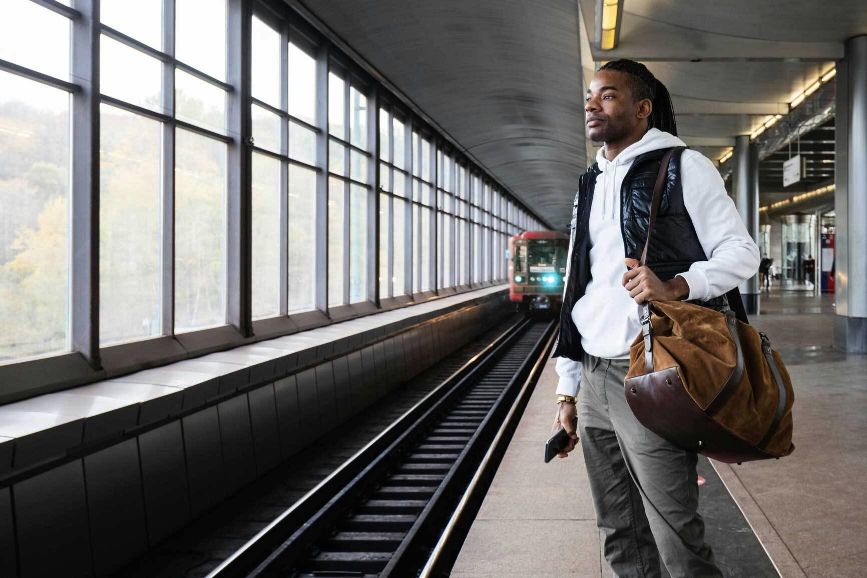A Millennial man stands on a subway platform waiting for the train
