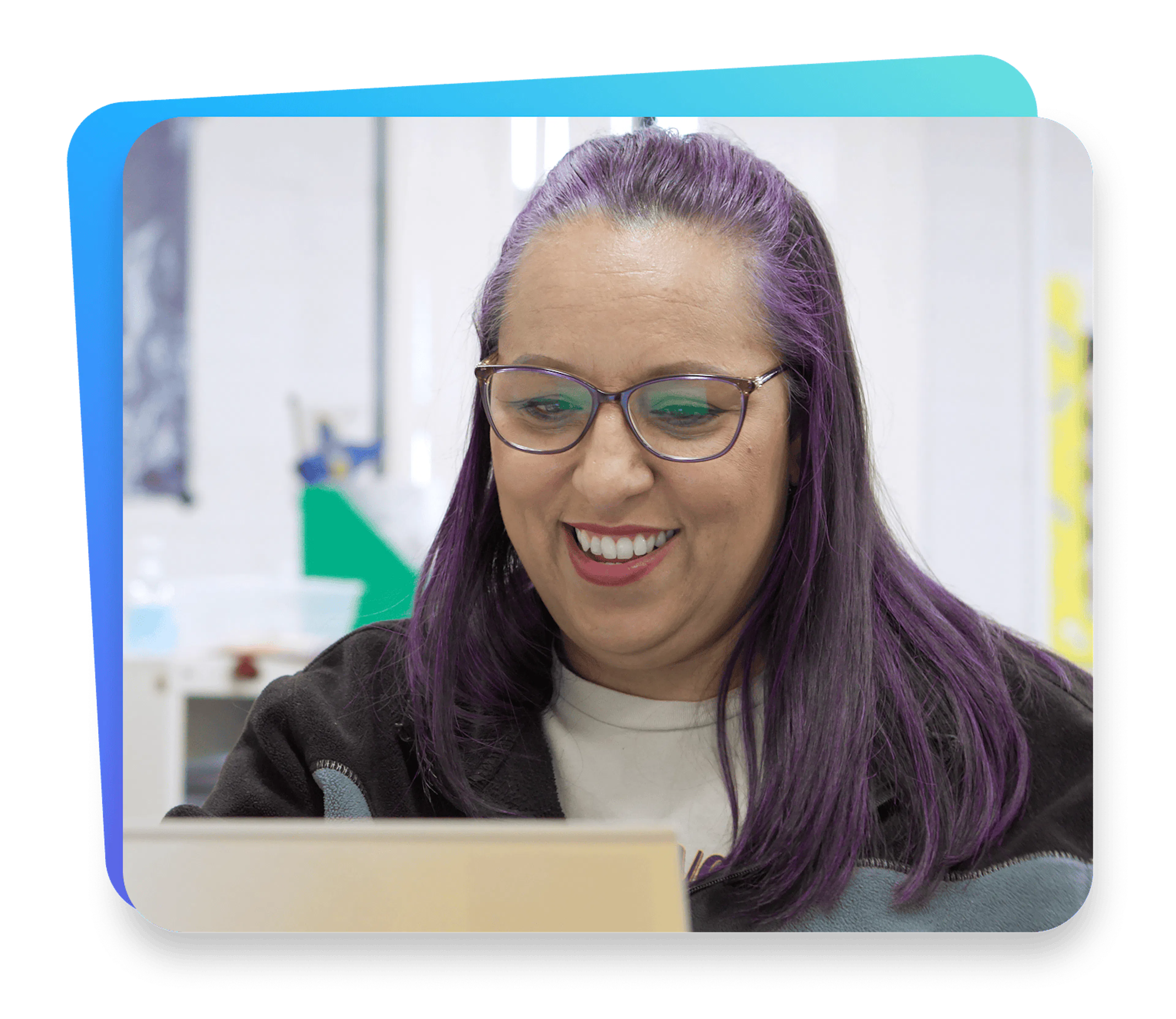 Educator smiling while working on a laptop in a bright classroom.