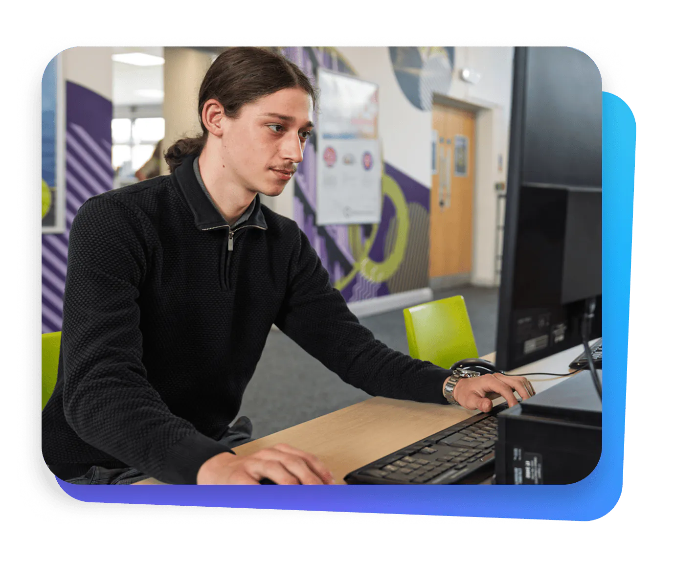 Student using a desktop computer in a campus learning space, focused on completing work, illustrating the use of AI and technology in higher education.