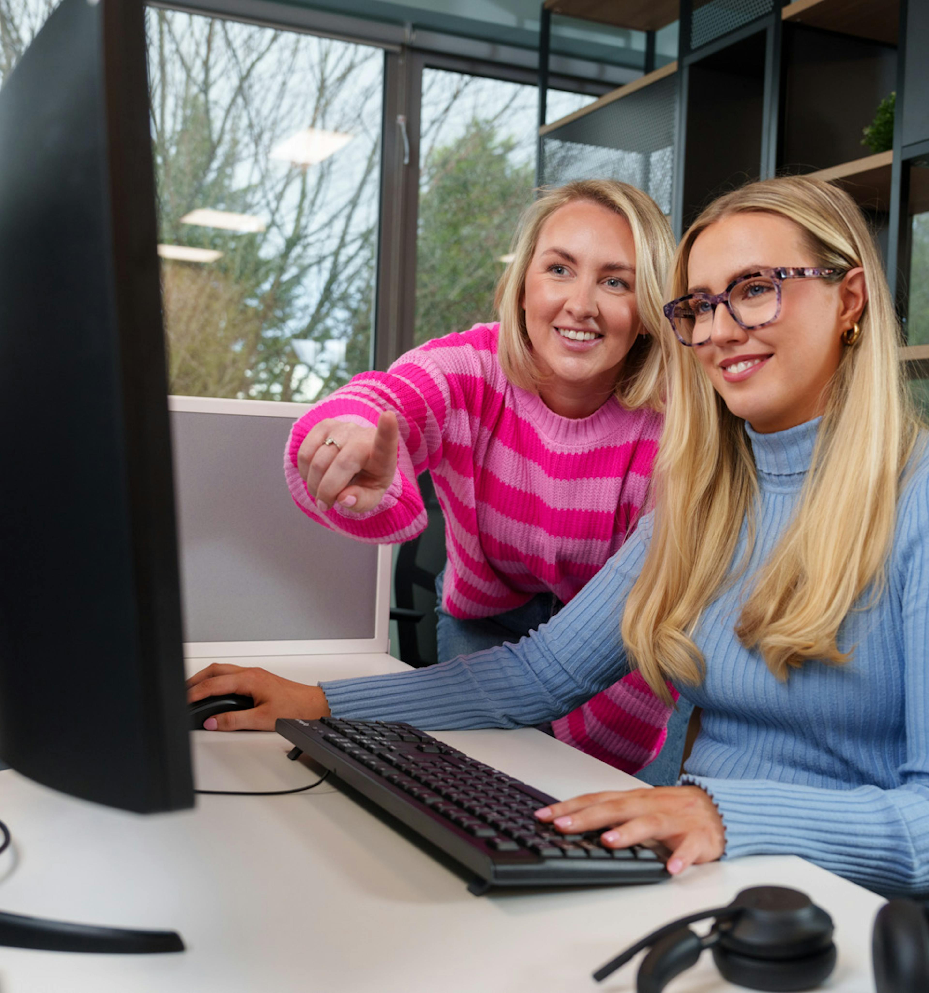 Two office employees are working together whilst looking at a screen, one is pointing. 