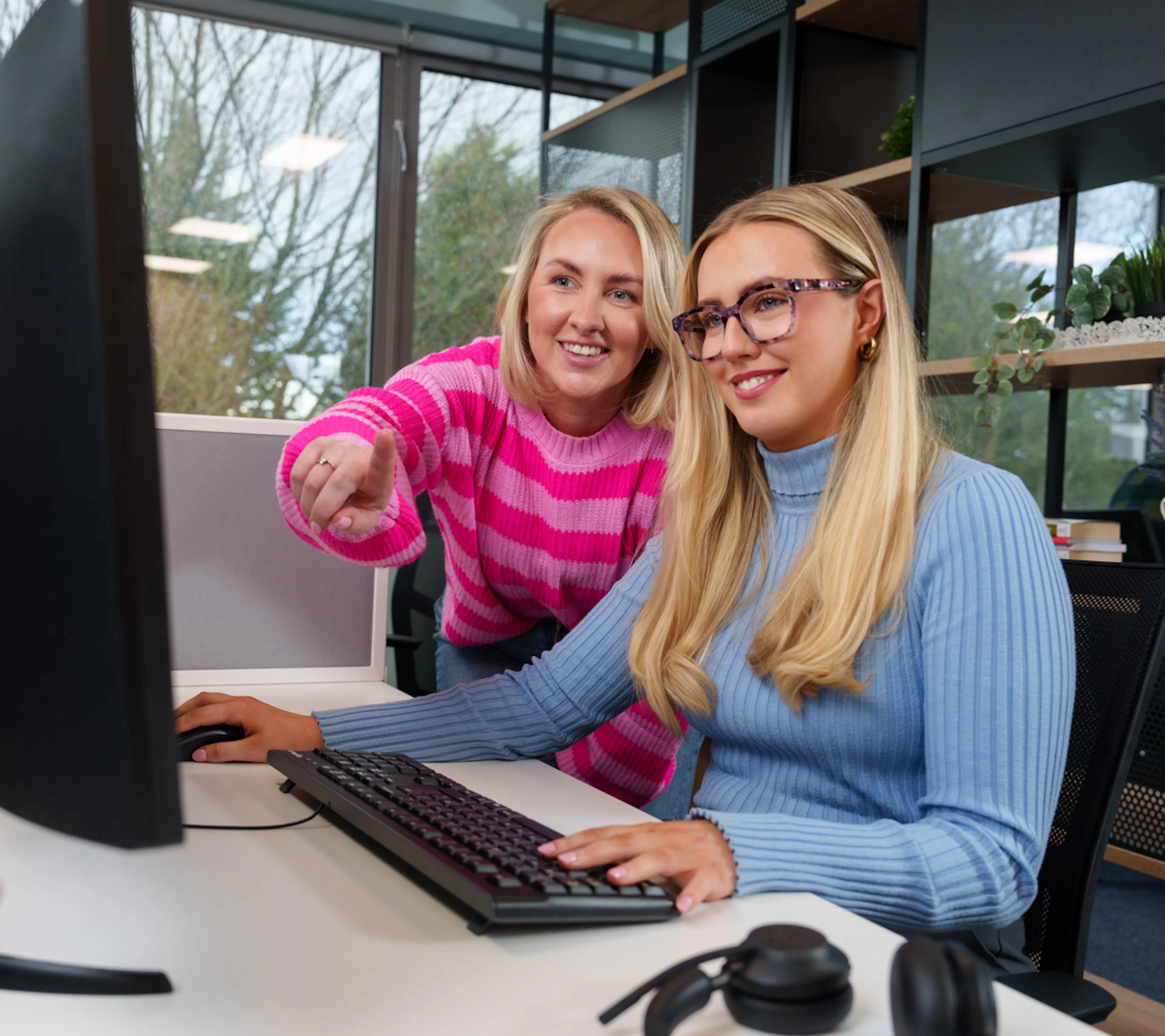 Two office employees are working together whilst looking at a screen, one is pointing. 