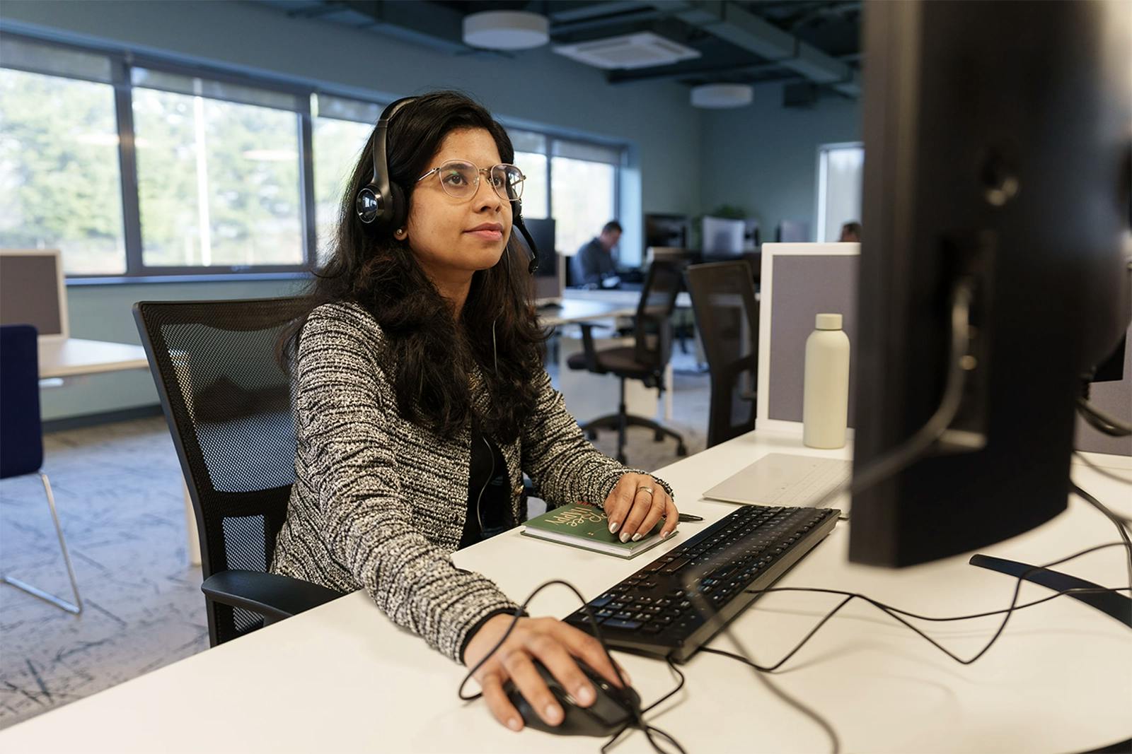 An employee wearing glasses and a headset using a computer in an office