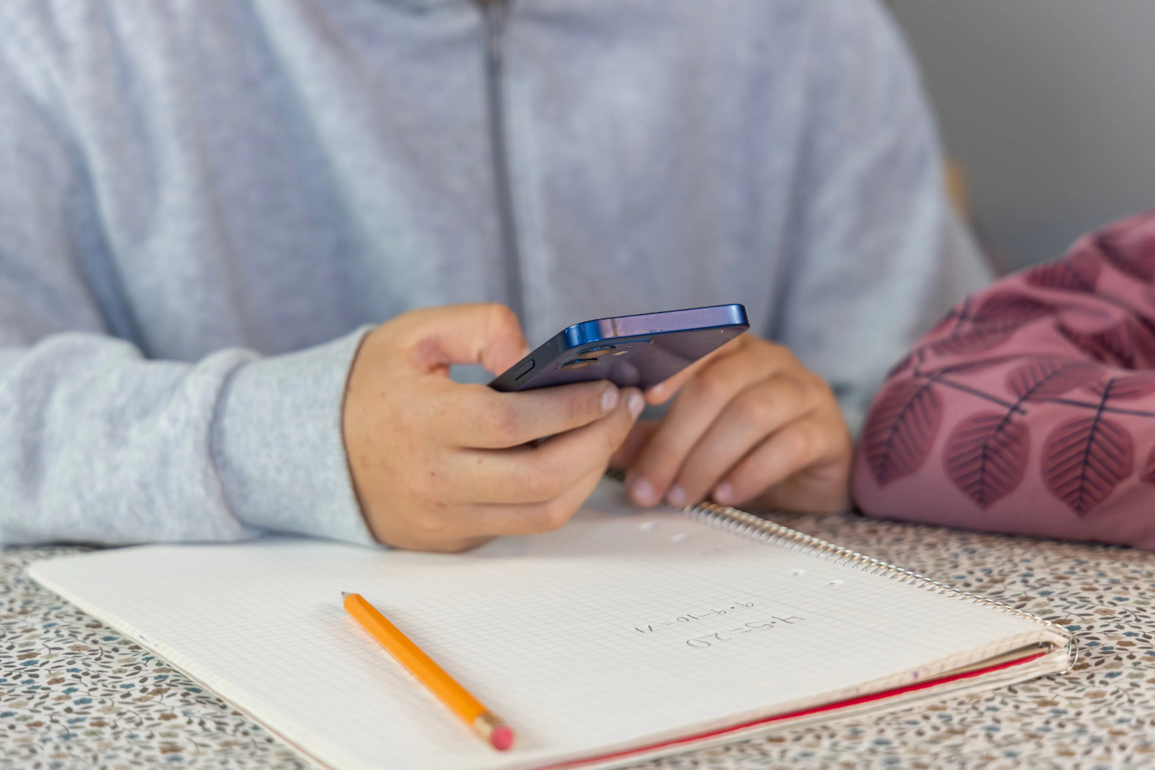 a child using a phone with a notebook and pencil underneath it