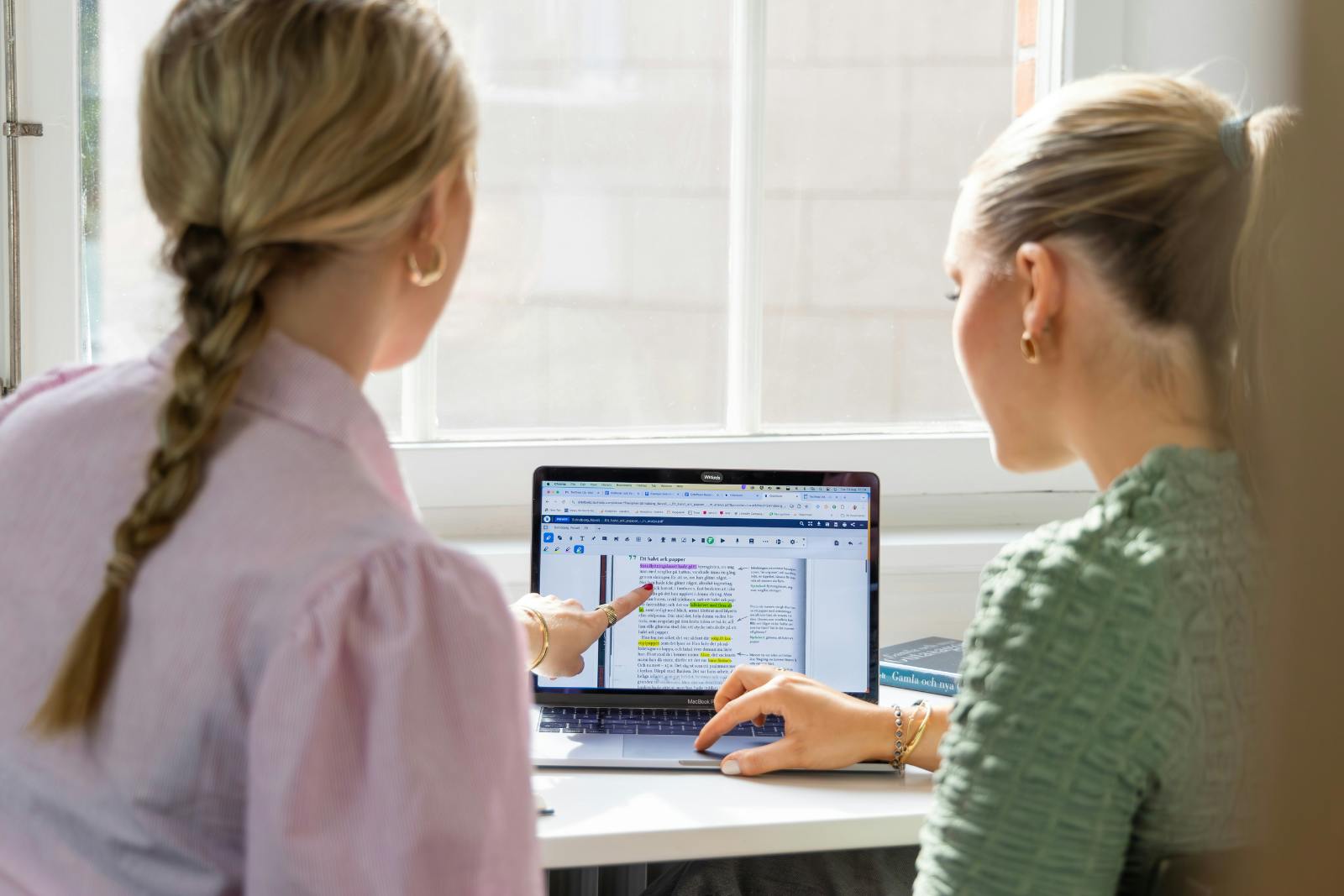 two girls pointing at a single laptop