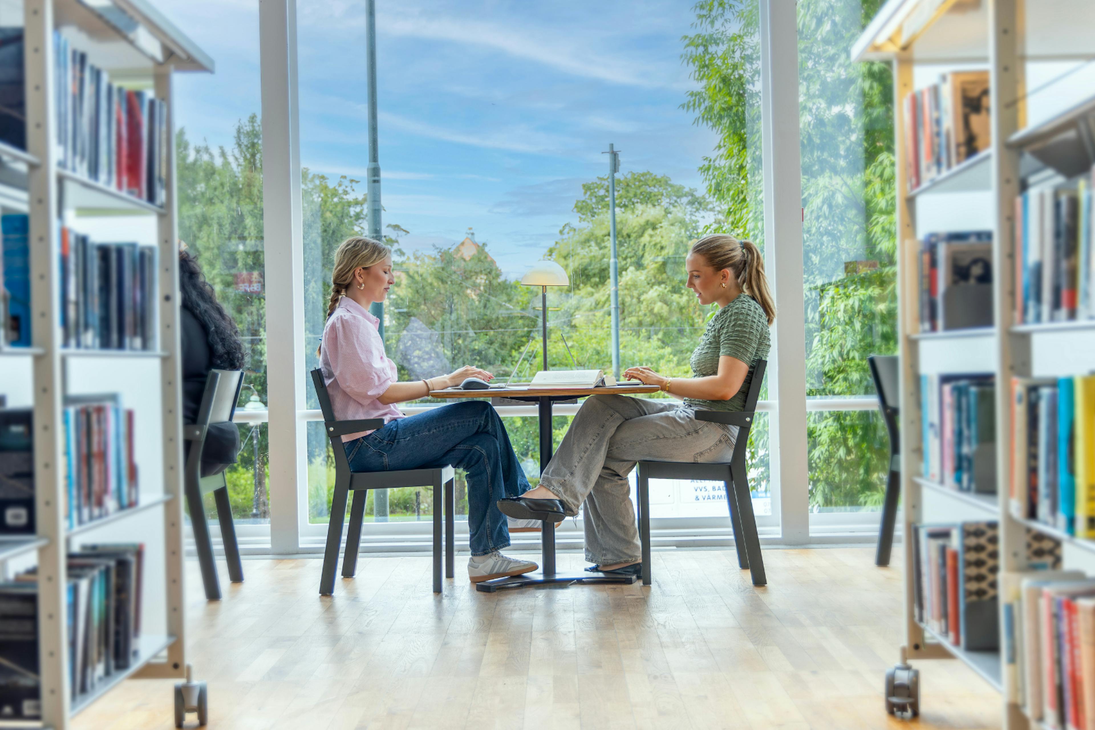 two girls sitting facing each other in a library