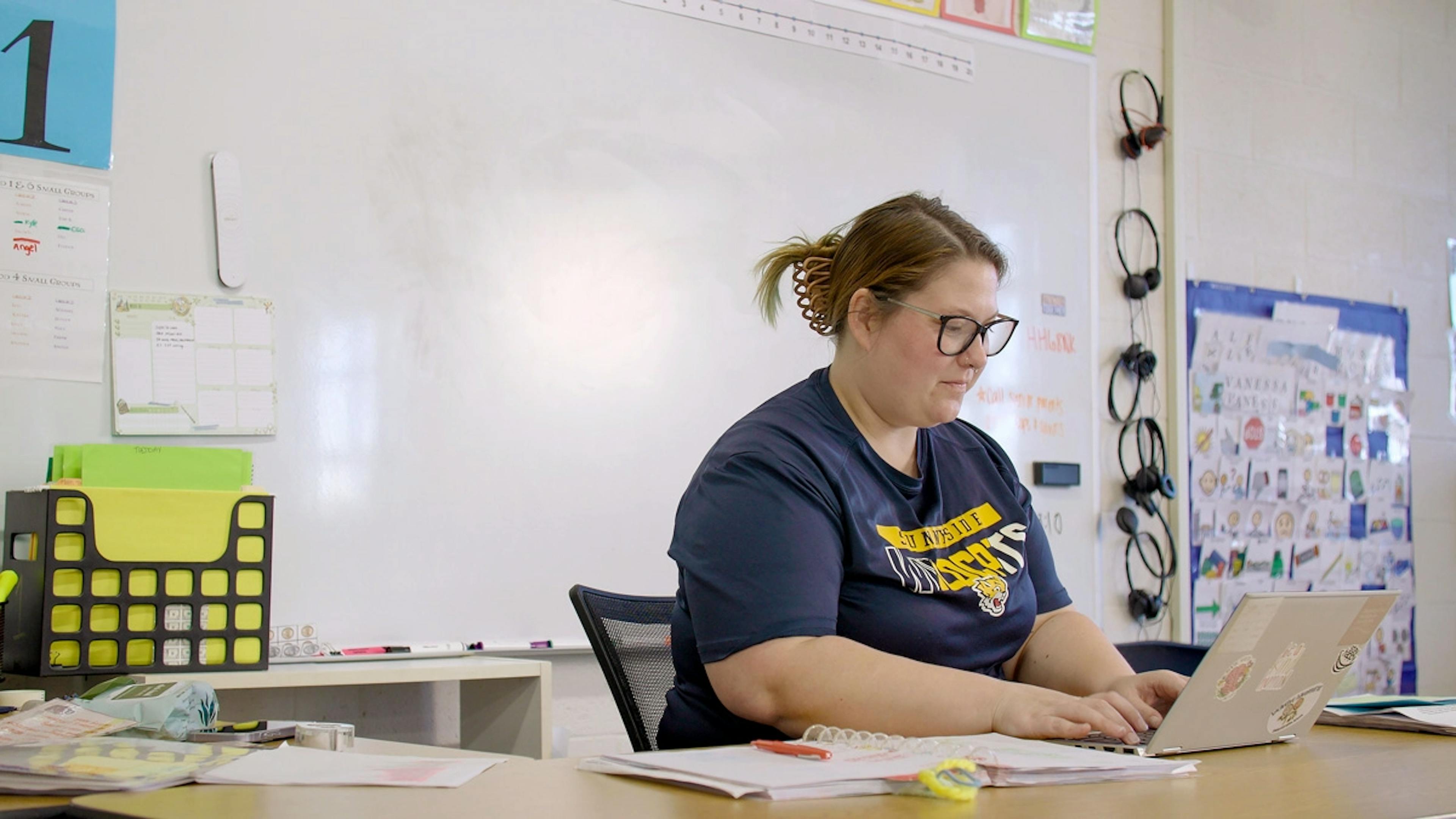 Educator in a classroom looking at a laptop