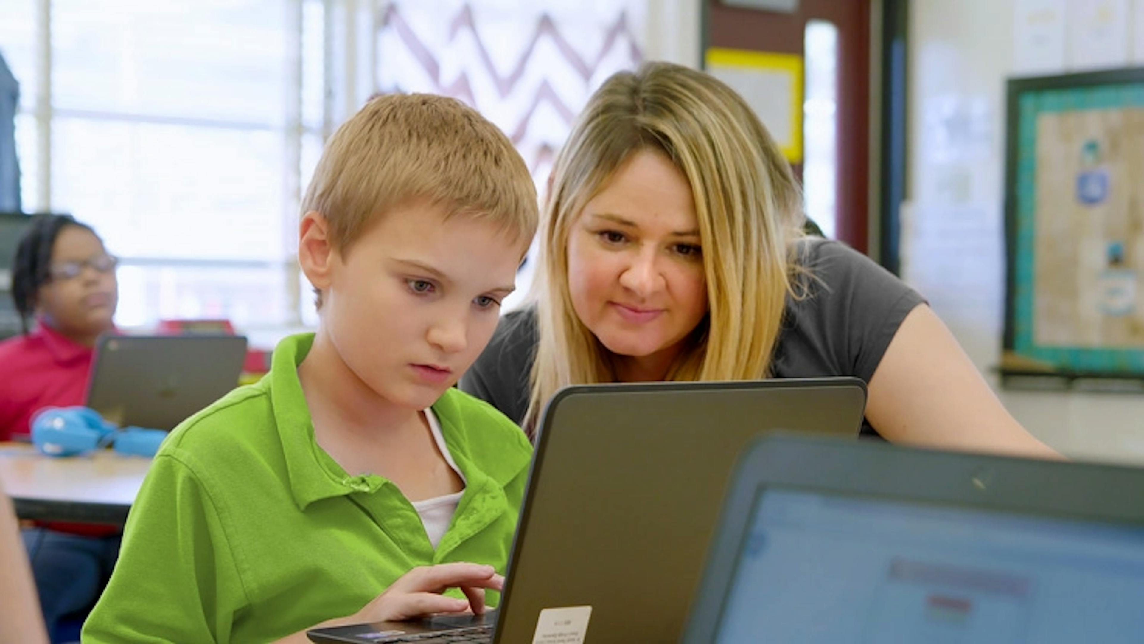 A teacher working with a student in school at a laptop