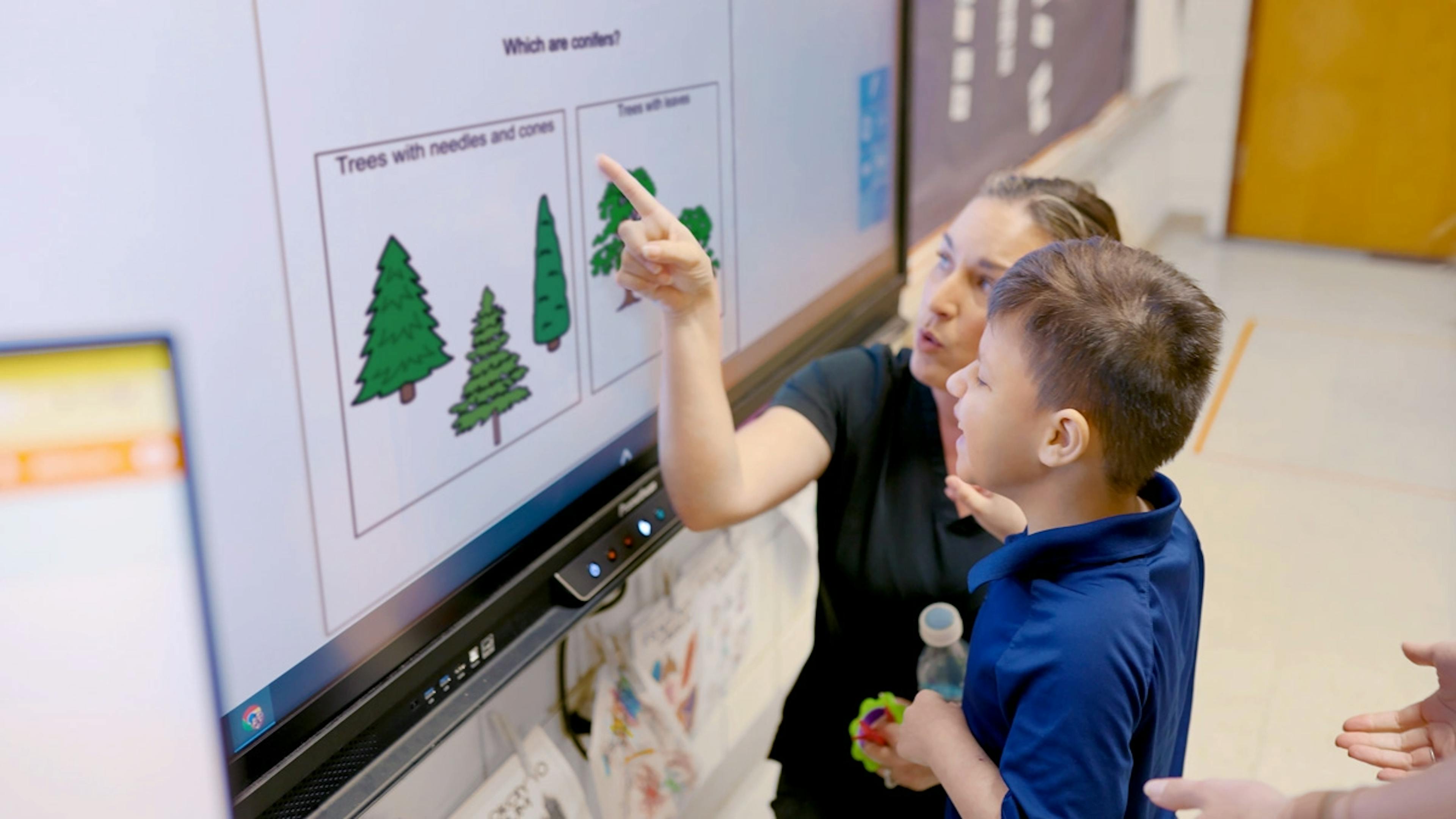 Teacher and student interact with a touchscreen displaying tree diagrams.
