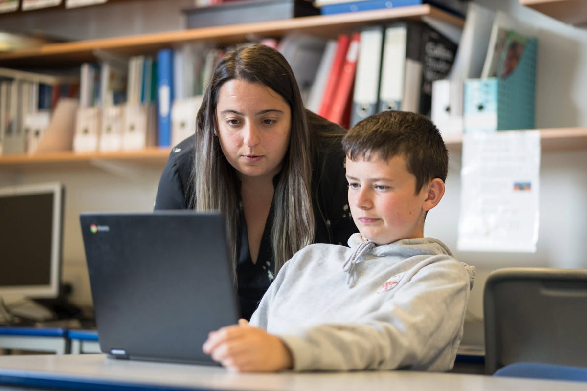 En lärare och en elev tittar på en laptopskärm