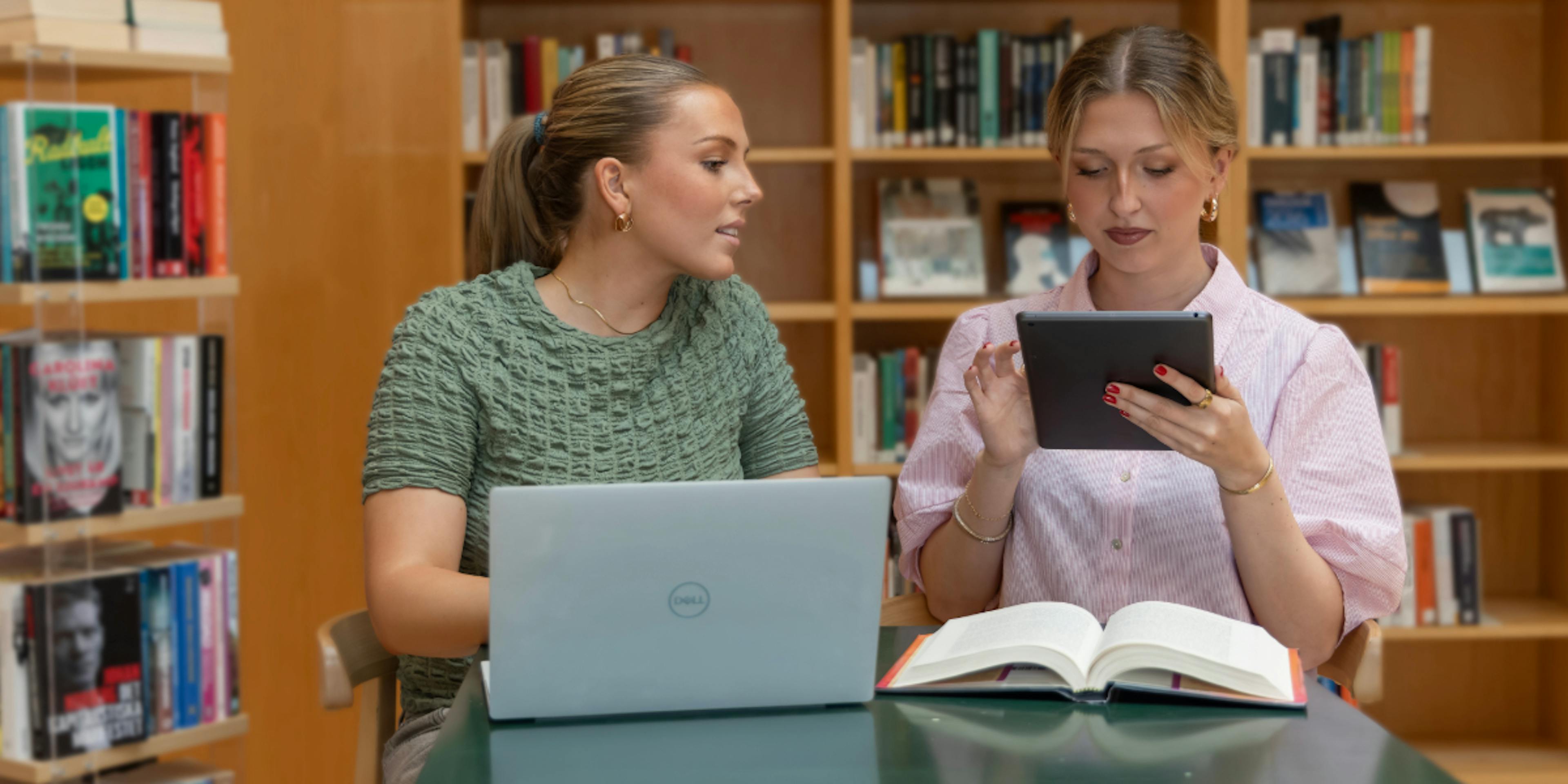 Two students in a library with devices