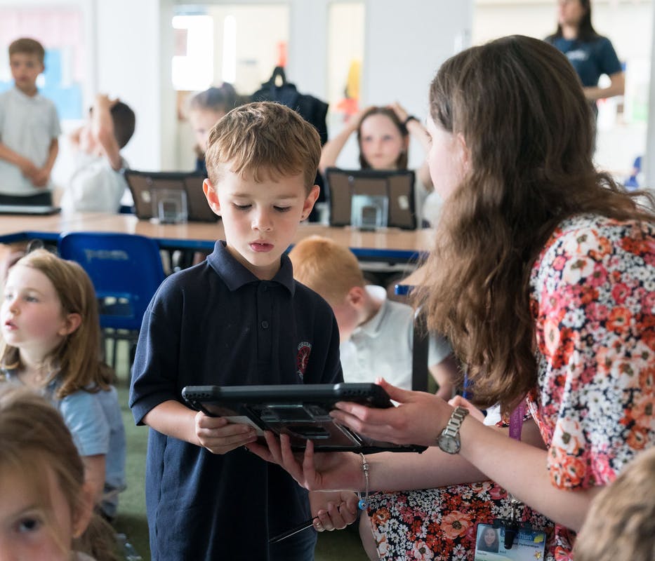 A student in a busy classroom with a teacher or classroom assistant