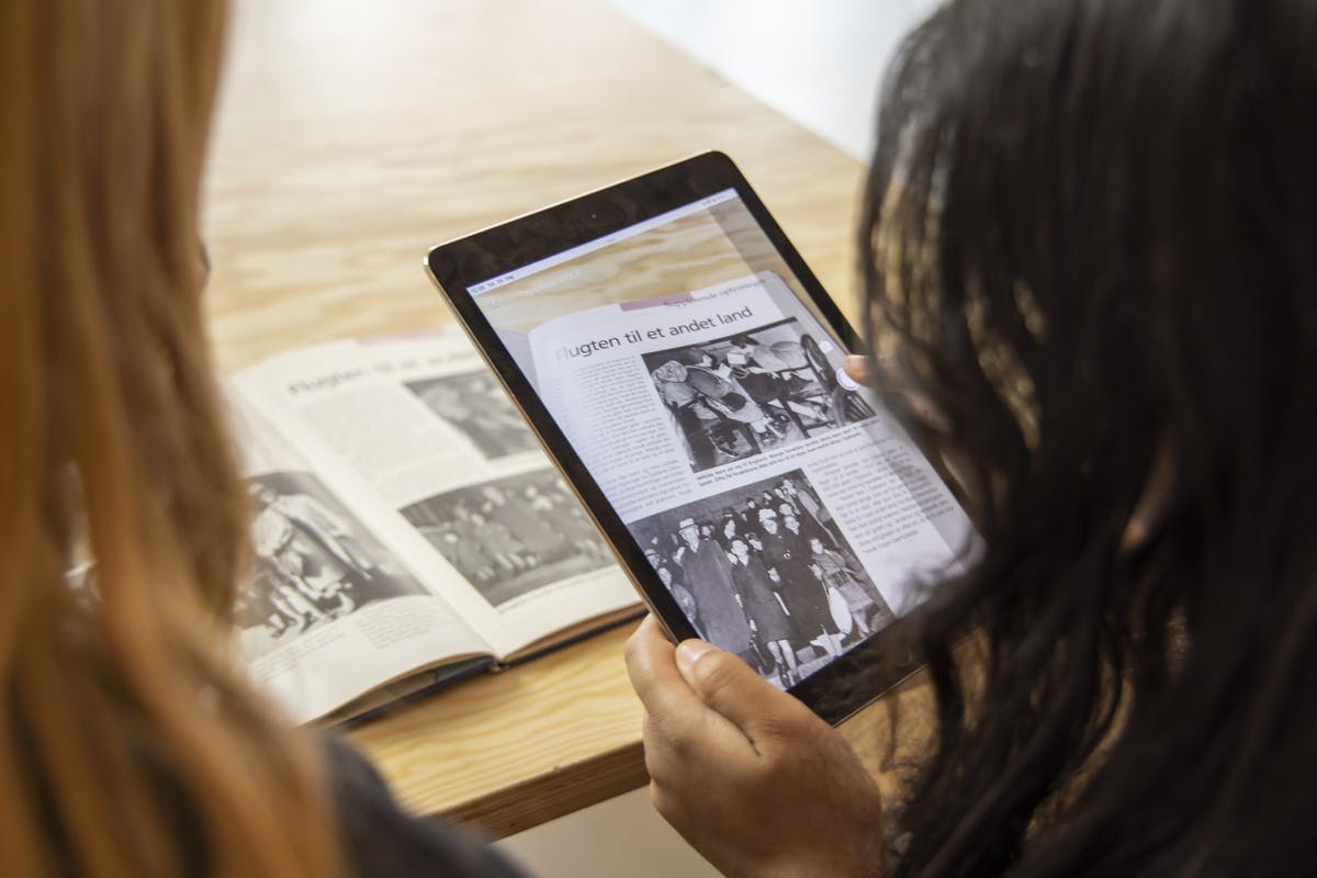 Two people looking at a textbook together, one taking a picture of the page on a tablet.