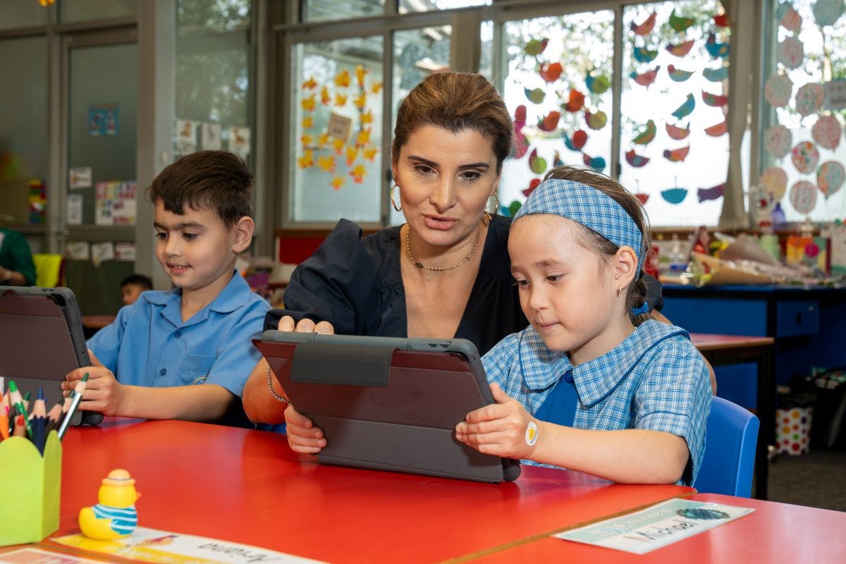 A teacher with two young students on iPads