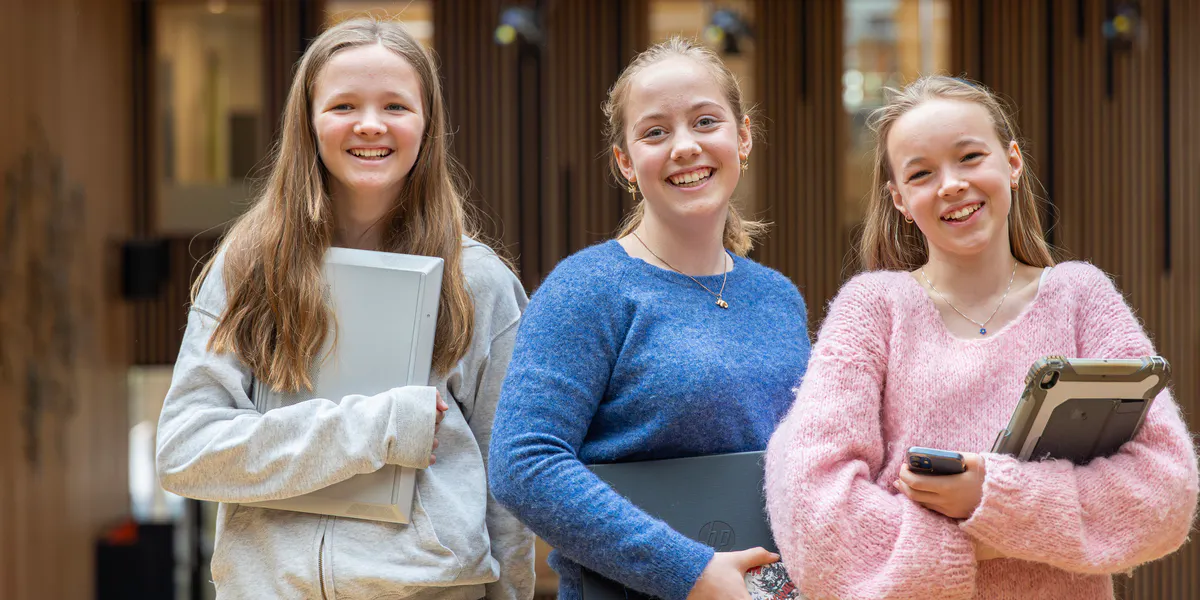Three students smiling at the camera, all holding laptops