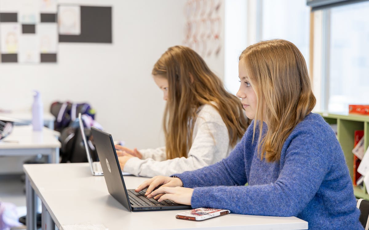 To studenter sitter i et klasserom med bærbare datamaskiner